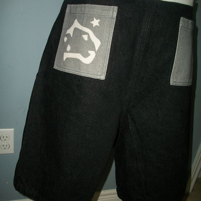 Black shorts with a white logo on the back pocket against a blue wall.