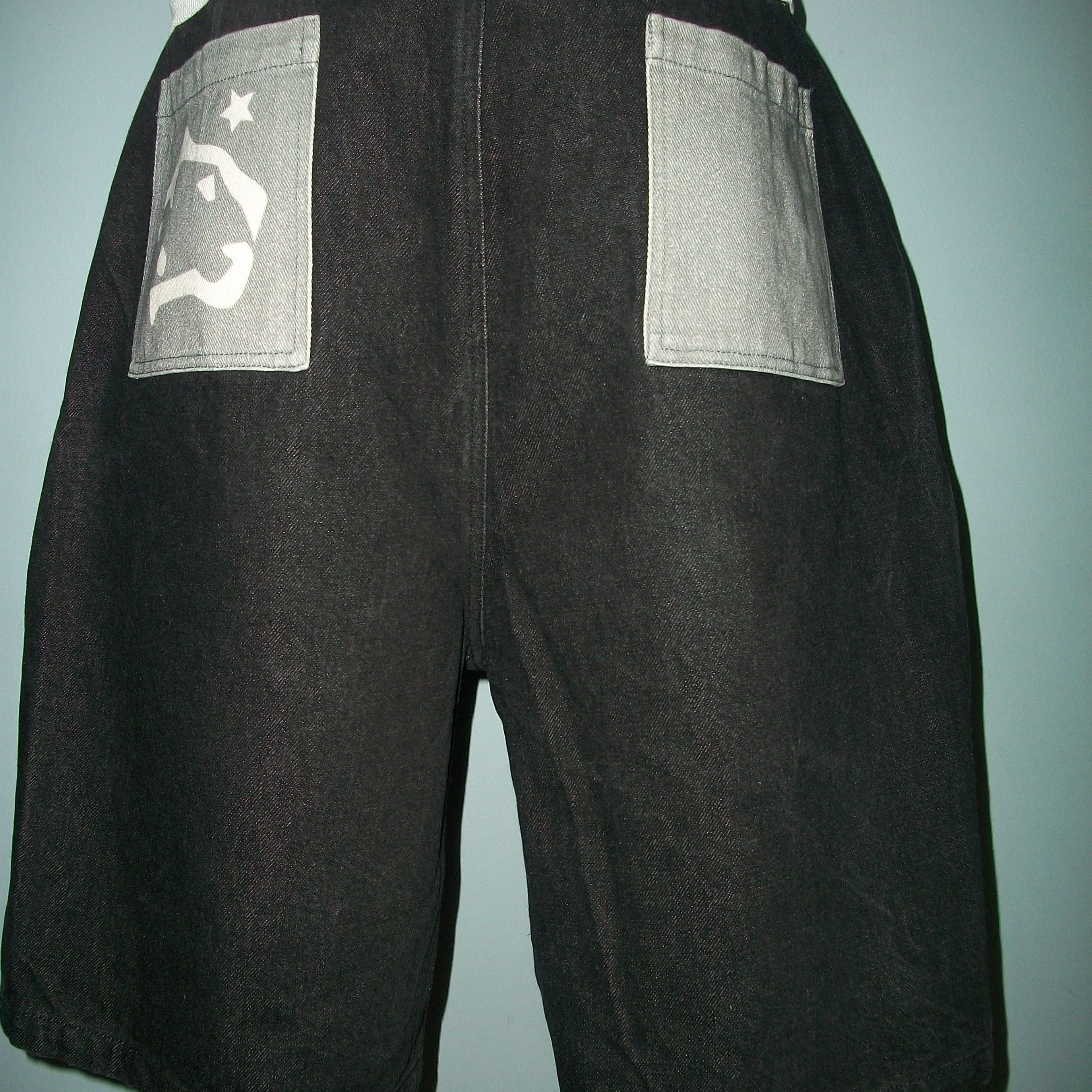 Black shorts with a patch on a person against a light blue wall